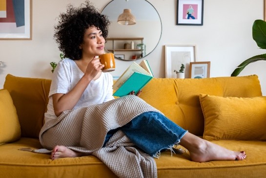 Person on a couch with a mug and a book